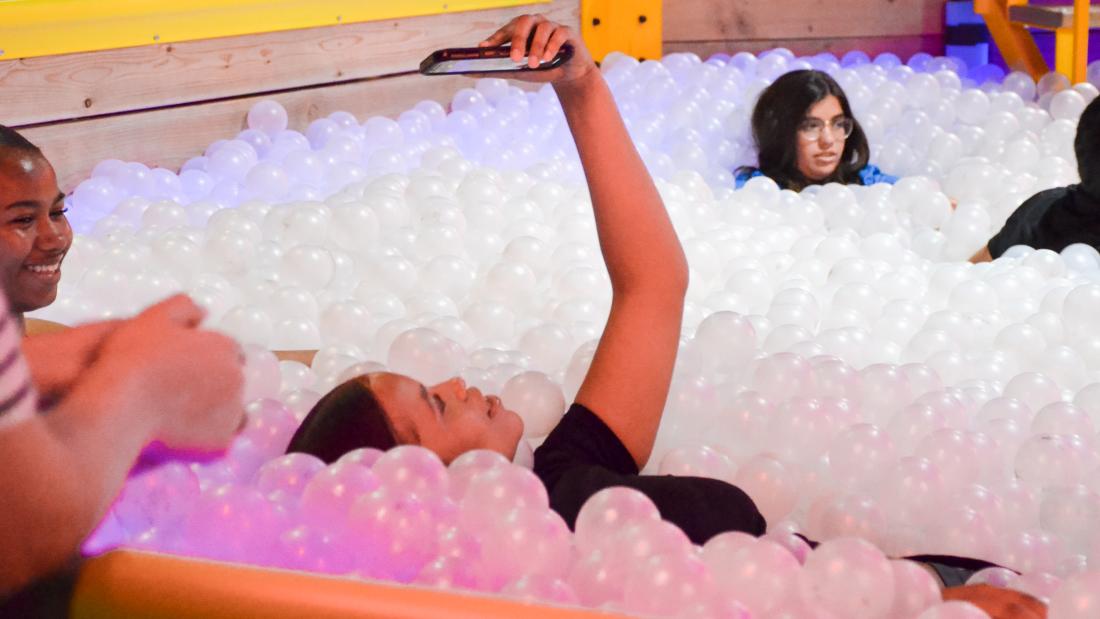 A woman laying in a white ball pit taking a selfie