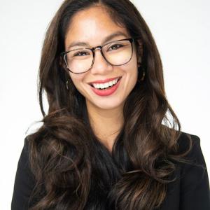An asian woman with glasses wearing a dark outfit 